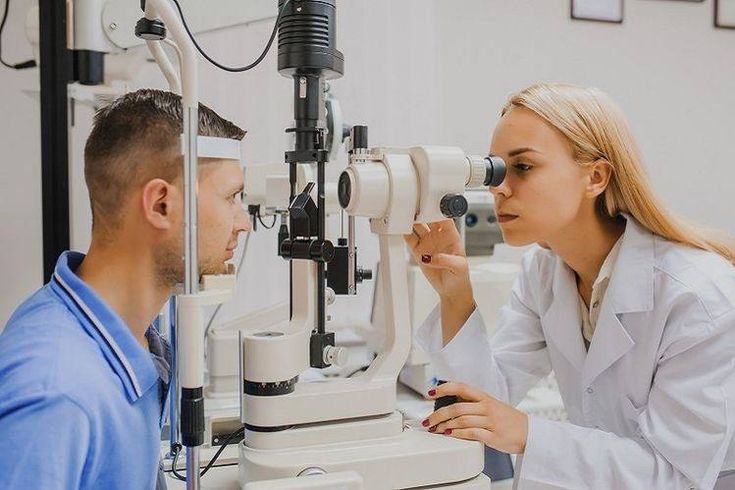 Eye doctor performing an eye exam using a slit lamp microscope on a patient, representing ophthalmology clinics that rely on secure IT systems and EMR support from predictiveIT.