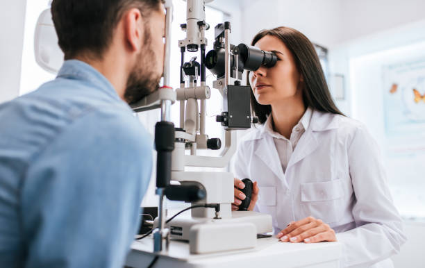 Female optometrist performing an eye exam on a patient using a slit lamp microscope in a clinic.