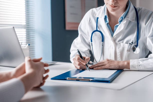 Doctor consulting with a patient while reviewing medical documents and writing notes in a modern healthcare office setting.