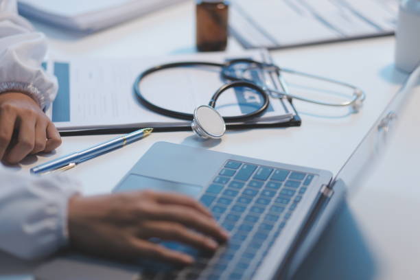 Healthcare professional using a laptop at a medical workstation with a stethoscope and patient documents, representing digital healthcare and secure medical IT systems.